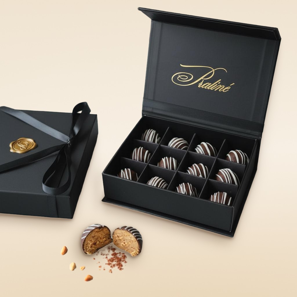 A Praline gift box of chocolate peanut butter truffles with white chocolate stripes, one truffle cut open to show the peanut butter center